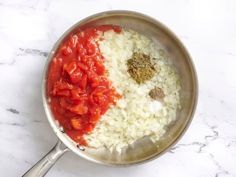 Add the diced tomatoes (with their juices), oregano, basil, crushed red pepper, salt, and black pepper. Stir in the tomato paste and water until fully combined.