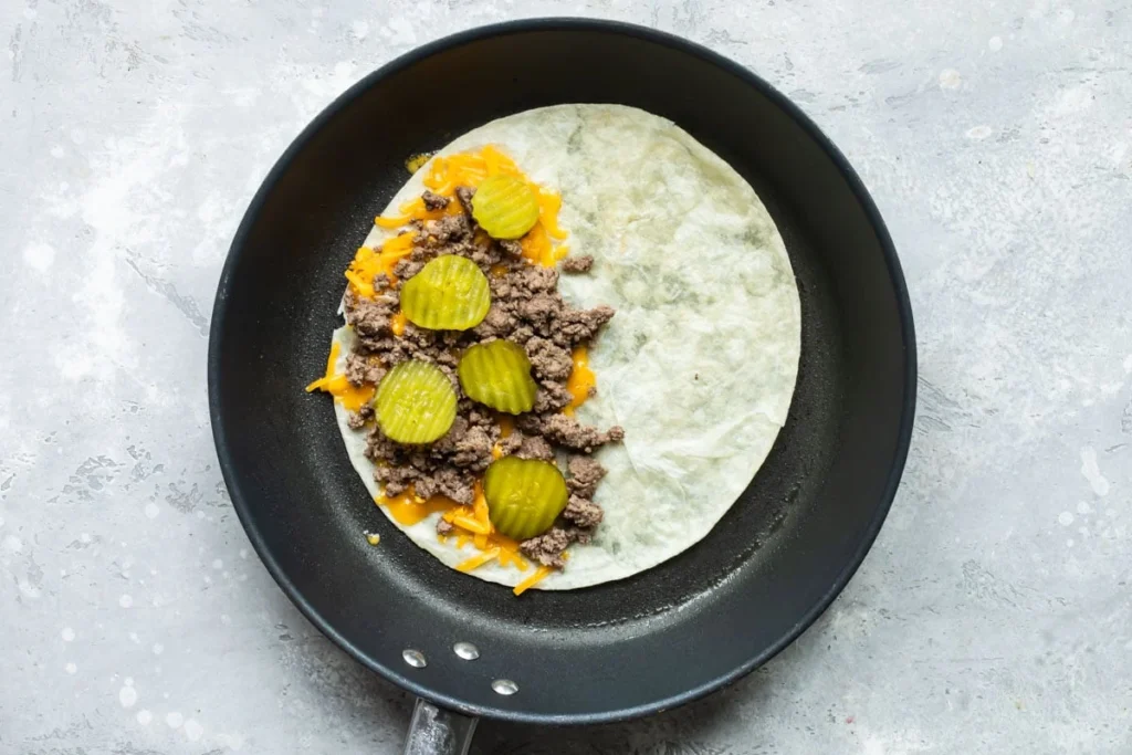 On one half of the tortilla, sprinkle ½ cup of shredded cheese. Add ¼ of the cooked beef on top of the cheese. Add pickle slices if using. Sprinkle another ½ cup of cheese over the beef.
