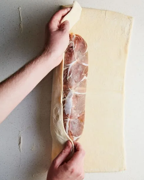 Unwrap the roast and place it seam-side down on the bottom edge of the pastry. Roll tightly until fully wrapped. Brush the edge with egg wash just before sealing. Trim any extra pastry and press the seam to seal.