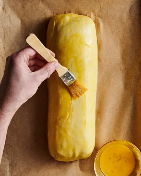 Fold the ends of the pastry over to cover the roast completely, brushing with egg wash where it folds to help seal. Trim excess if needed. Transfer to the baking sheet seam-side down. Brush the whole pastry with egg wash.