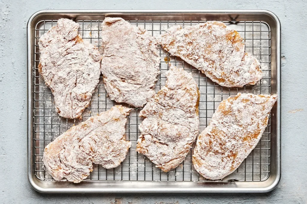 Working with one piece at a time, dip the chicken into the eggs, turning to coat and letting any extra drip off. Then press both sides into the flour mixture so it sticks well. Place each coated piece on the rack and let it sit for at least 15 minutes.