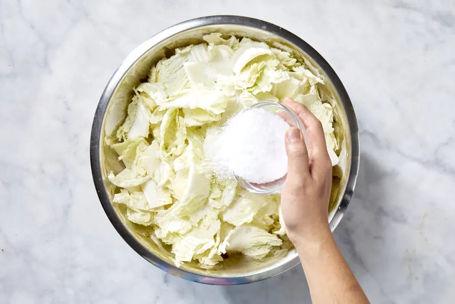 Place the cabbage in a large bowl and sprinkle with the salt. Use your hands to gently massage the salt into the leaves until they begin to soften. Add enough water to fully cover the cabbage. Place a plate on top and weigh it down with something heavy. Let it sit for 1 to 2 hours.