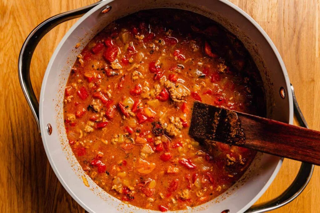 Add the fire roasted tomatoes with their juices, beef broth, chopped roasted red peppers, and 1 to 2 cans of diced green chiles. Stir well and bring to a boil over high heat. Reduce to a simmer and cook for 5 minutes.