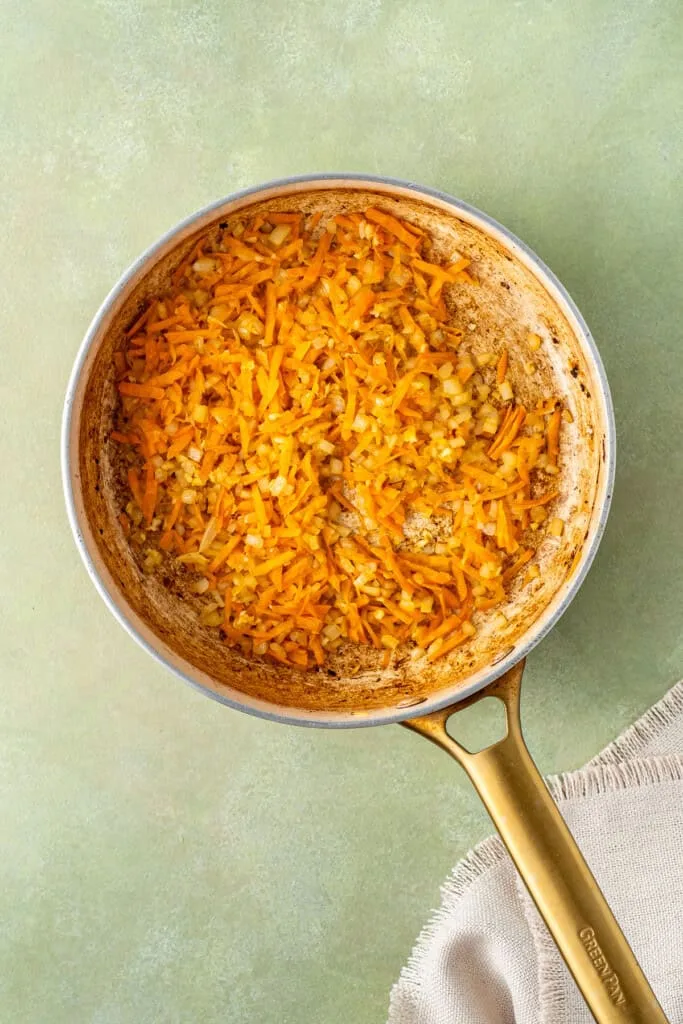 In the same pan, cook the onion until translucent, then add the grated carrot and minced garlic, continuing to sauté until everything is soft and fragrant.
