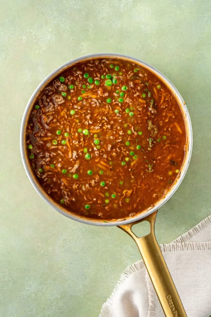 Return the beef to the pan, stir through the vegetables, then add the flour and cook briefly before mixing in the tomato paste to build a rich base.