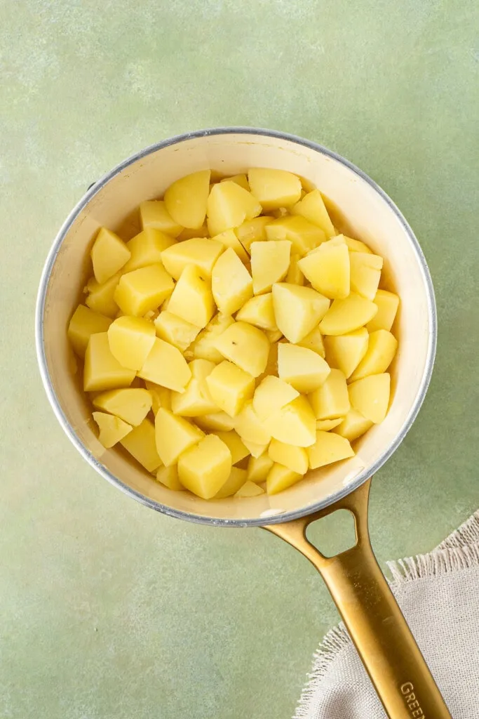 Peel and chop the potatoes, place them in a saucepan with water, and bring to a boil while preheating the oven to 200°C.