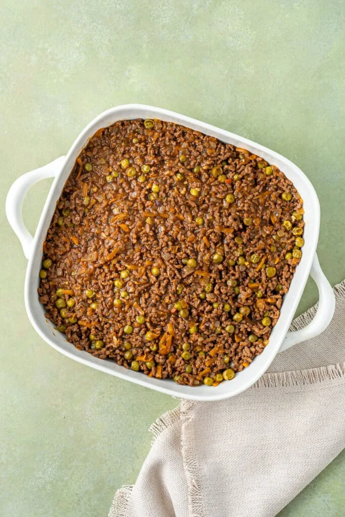 Transfer the beef filling into a casserole dish and spread it evenly, then layer the mashed potatoes on top and smooth the surface with a spoon.