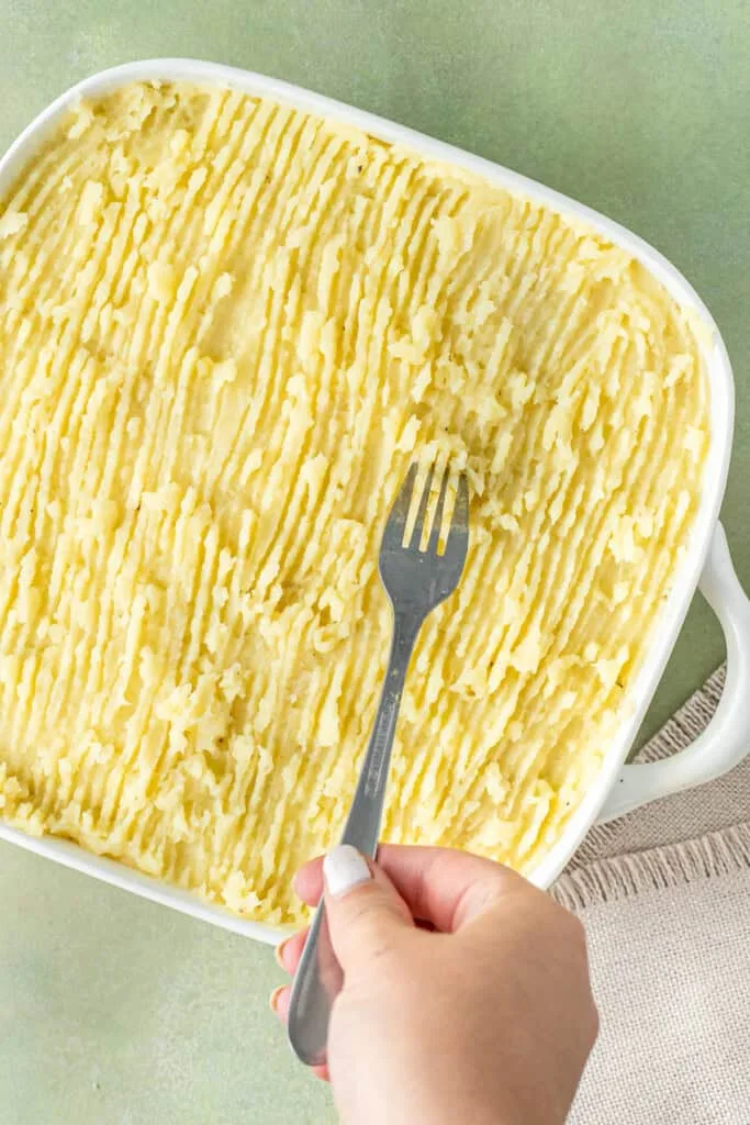 Score the mashed potatoes with a fork to create texture, then bake until the top is golden and the filling is bubbling around the edges.