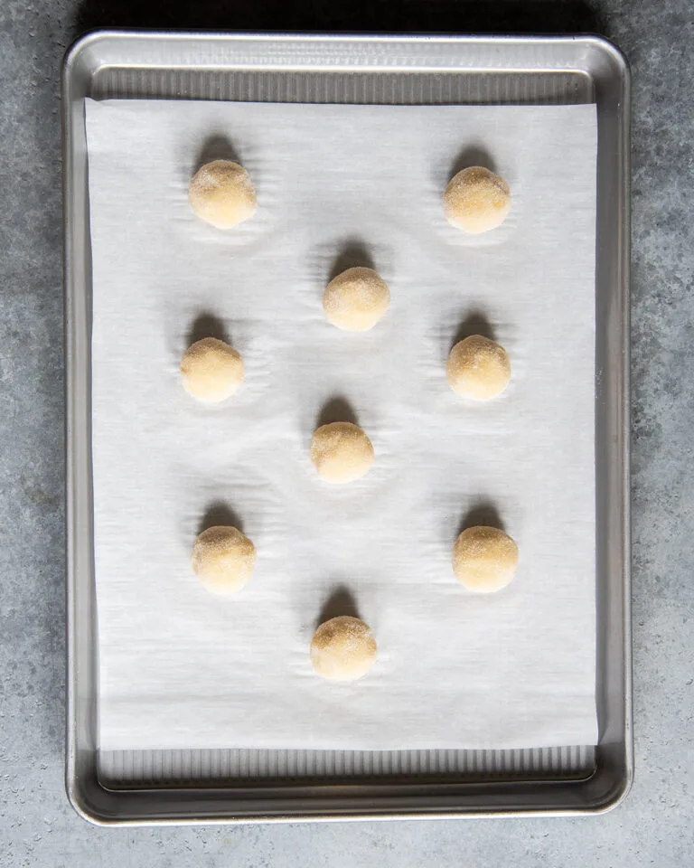 Scoop the dough into even portions and roll them into balls, then coat each ball in granulated sugar for a lightly crisp exterior.