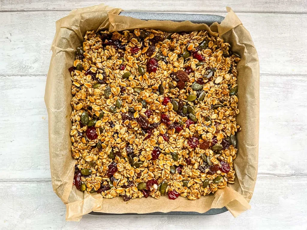 Line a baking tray with baking paper, transfer the mixture into the tray, and press it down firmly and evenly, making sure it reaches all corners.