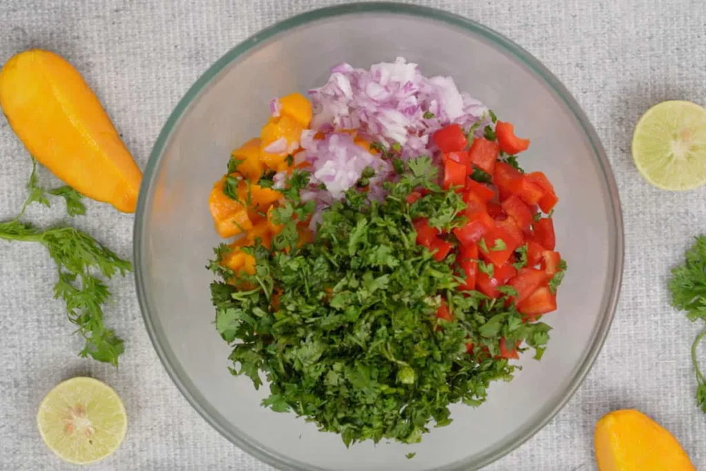 Remove the bowl from the refrigerator and add the diced mango, chopped onion, jalapeño, bell pepper, and cilantro.