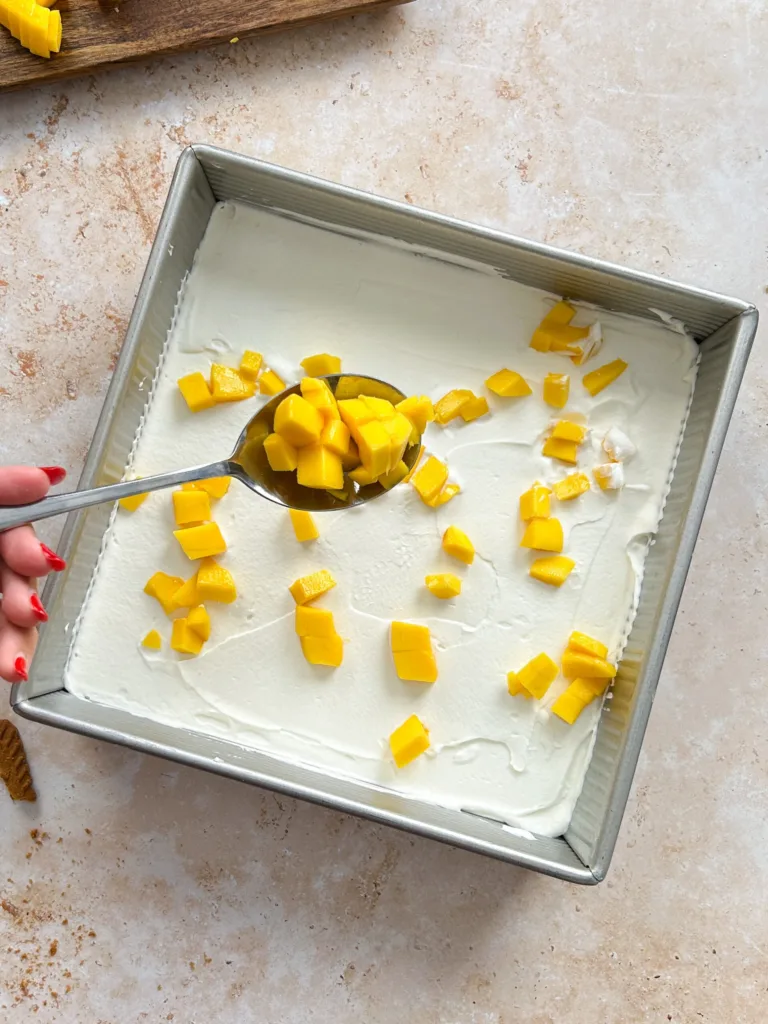 Finish with a final layer of cookies and the remaining cream, then decorate the top with mango slices and crushed cookies for added texture.