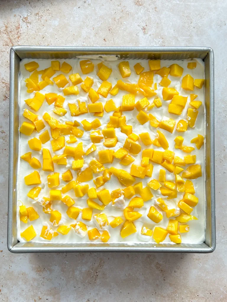 Finish with a final layer of cookies and the remaining cream, then decorate the top with mango slices and crushed cookies for added texture.